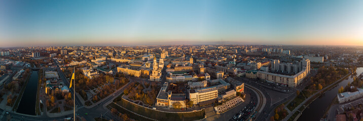 Obraz premium Sunny autumn cityscape, city streets traffic. Wide panoramic aerial view above river Lopan embankment, Flagpole with flag of Ukraine, Pavlivska Square, Dormition Cathedral in Kharkiv, Ukraine