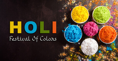 Happy holi festival decoration.Top view of colorful holi powder on dark background with the text.