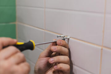 Man hands with screwdriver screwing nails into dowels hammered into tiled wall in washroom. Renovation works in bathroom. Dirt from renovation process.