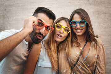Three funny student friends looking with colorful eyeglasses - Portrait of three young friends...
