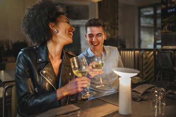 Happy romantic biracial couple of young people meeting in the restaurant while drinking white wine