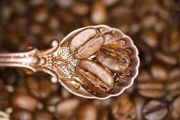 Top down view on isolated vintage bronze spoon with 3 roasted coffee beans, blurred background  - selection of best good coffee sort concept - obrazy, fototapety, plakaty