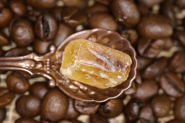 Closeup of vintage bronze spoon with one single cube brown rock candy sugar, blurred roasted coffee beans background