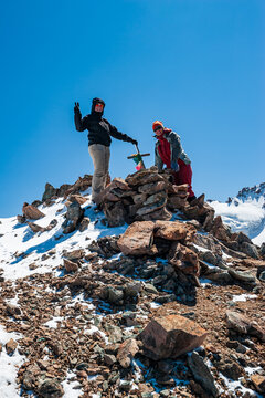 Two young women trekkers standing on top of Pik Uchitel peak with cross. Ala Archa Alpine National Park Landscape near Bishkek, Tian Shan Mountain Range, Kyrgyzstan, Central Asia.