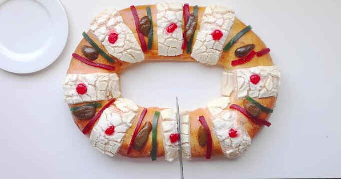 A person cutting a Rosca de Reyes - Three Kings Bread on a white table