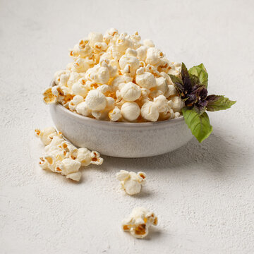 Salted popcorn in a ceramic plate with basil and scattered on the table. Square image of erving snacks