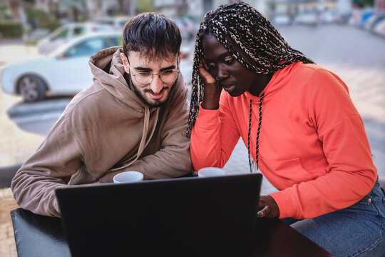 Biracial couple using laptop sitting at outdoors cafe restaurant