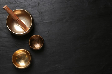 Golden singing bowls and mallet on black table, flat lay. Space for text