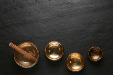 Golden singing bowls and mallet on black table, flat lay. Space for text