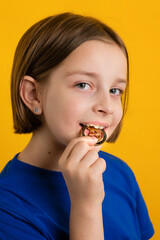 Little Girl 8-10 Years Old in Basic Blue T-shirt Biting Golden Physical Bitcoin on Yellow Background. Children Financial Literacy. Cryptocurrency and blockchain concept.