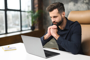 High angle view of the concentrated man looking at the laptop screen with serious expression while looking from the office. Serious guy at work