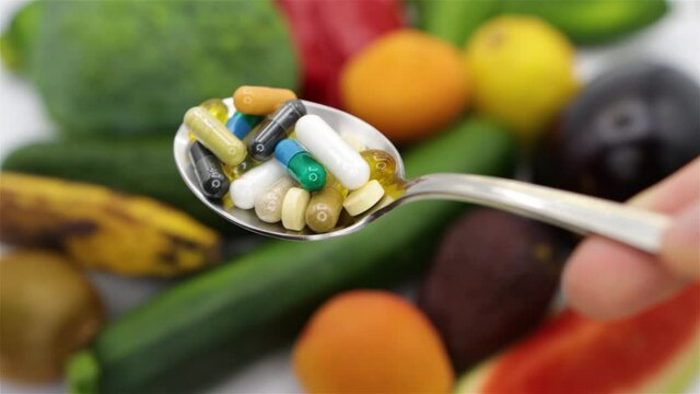 Capsules and pills of nutritional supplements and fresh vegetables and fruits background, concept of healthy life and supplementation