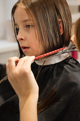 Child gets her haircut from Hairdresser in beauty salon. Little girl with short bob hair....