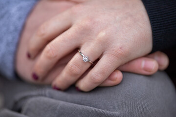 Closeup of couple holding hands with engagement ring. Single solitaire diamond engagement ring.  