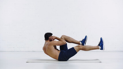 Fototapeta premium full length of shirtless sportsman doing abs exercise on fitness mat near white brick wall