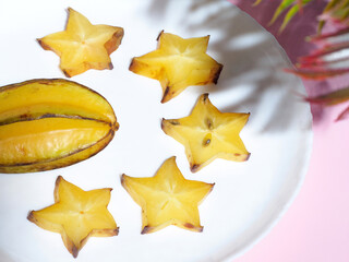 Fototapeta premium Cut and whole carambolas on white background. Flat lay composition with carambolas on color pink background. Top view. Yellow exotic tropical fruits. Copy spase. Space for text. Thai fruits. Close up