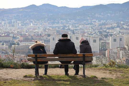 Three people on a bench watch the view from the hill over the city of Clermont-Ferrand