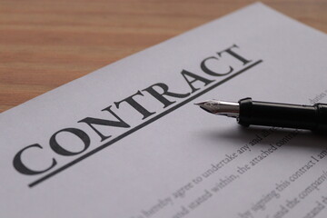 Fountain pen lain across contract paperwork against wooden table top 