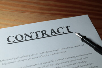 Fountain pen lain across contract paperwork against wooden table top 