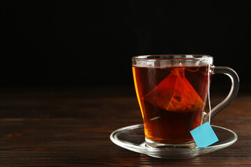 Tea bag in glass cup of hot water on wooden table. Space for text