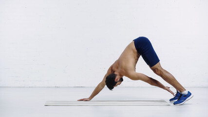 shirtless sportsman stretching back on fitness mat near white brick wall