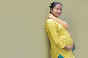 A pregnant Indian lady with a yellow dress and hands-on belly. Motherhood and pregnancy concept.