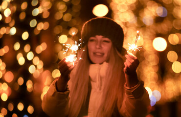 Young woman looks at the burning sparklers. In the background, the side of the Christmas city garlands