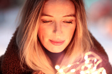 Young woman holds a garland in her hands and admires the bright lights. Portrait. Close-up