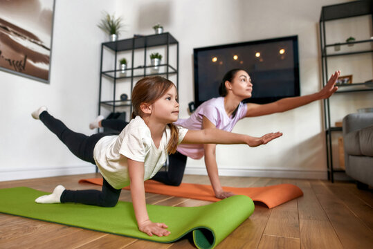 Sporty mom and small daughter do yoga at home