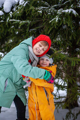 Fototapeta na wymiar Two sisters embracing against background of snowy fir tree
