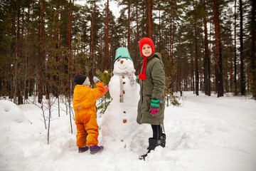 Two sisters making  snowman  in winter  forest