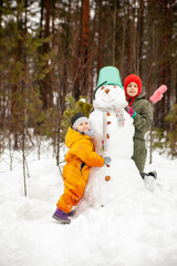 Fototapeta na wymiar Two sisters making snowman in winter forest