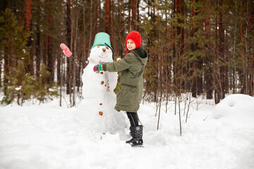 Fototapeta na wymiar Girl of nine years old on winter walk near snowman