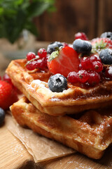 Delicious Belgian waffles, berries and powdered sugar on wooden board, closeup
