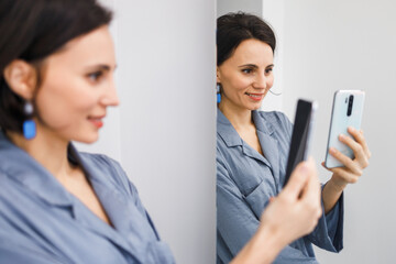 Bruinette woman in pajama working online with smartphone in hands at home. Female using phone looking at screen typing message, using telephone technology doing online job, surfing internet social