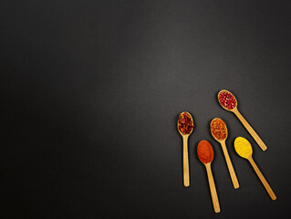 On a black background, on the right, there are four wooden spoons with spices.