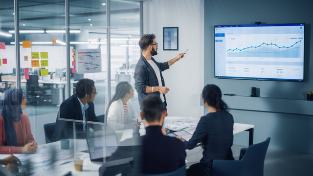 Diverse Modern Office: Motivated Businessman Leads Business Meeting with Managers, Talks, uses Presentation TV with Statistics, Chart Growth, Big Data. Digital Entrepreneurs Work on e-Commerce Project