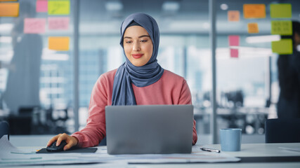 Modern Office: Portrait of Young Muslim Businesswoman Wearing Hijab Works on Laptop, Does Data...