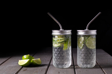Citrus non-alcoholic refreshing chilled drinks in glass bottles with lids and metal cocktail tubes on a black background.