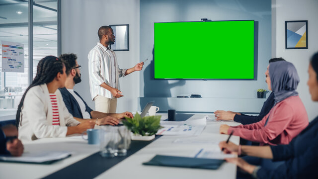 Office Conference Room Meeting Presentation: Black Businessman Talks, Uses Green Screen Chroma Key Wall TV. Successfully Presenting a Product to Group of Multi-Ethnic Investors. e-Commerce Strategy
