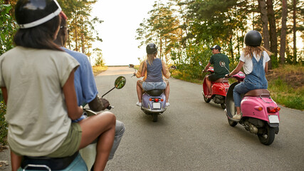 Rear view of young multiracial friends riding retro scooters