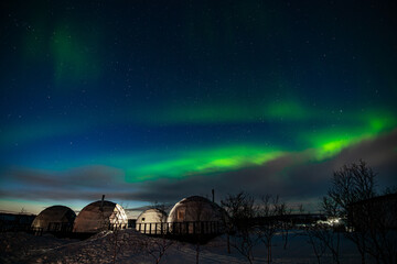 Fototapeta na wymiar Northern Lights also known as aurora, borealis or polar lights at cold night over igloo village. Beautiful night photo of magic nature of winter landscape