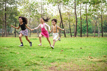 Fototapeta premium Small group of a happy children run through the park in the background of grass and trees. Children's outdoor games, vacations, weekend, Children's Day