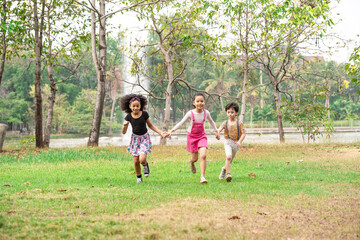 Obraz premium Small group of a happy children run through the park in the background of grass and trees. Children's outdoor games, vacations, weekend, Children's Day