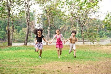 Fototapeta na wymiar Small group of a happy children run through the park in the background of grass and trees. Children's outdoor games, vacations, weekend, Children's Day