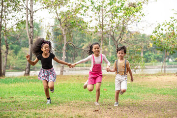 Obraz premium Small group of a happy children run through the park in the background of grass and trees. Children's outdoor games, vacations, weekend, Children's Day