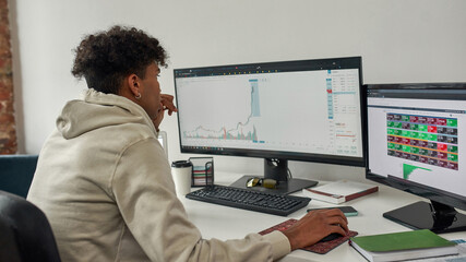 Fototapeta na wymiar Concentrated young male trader looking at computer screen, studying charts while trading from home