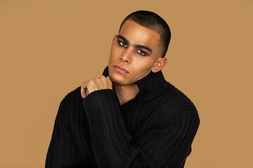 Closeup portrait of a handsome young Latin man with short hair, light makeup and eyeshadow sitting...