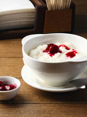 Plate of rice porridge with cherry jam on wooden table. Breakfast at the hotel, cafe, restaurant. Copy space. Morning. Food photography. Russian breakfast. Milk porridge for children. Proper nutrition
