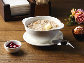 Plate of porridge with cherry jam, cake and butter on wooden table. Breakfast at the hotel, cafe, restaurant. Copy space. Morning. Food photography. Russian breakfast. Milk porridge for children. 